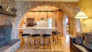 A kitchen with a brick arch, wooden bar stools, and a stone fireplace. - Riverside Condo in Downtown Winter Park! (Winter Park)