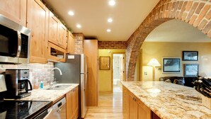 A kitchen with wooden cabinets, a granite countertop, a brick archway, and a view into the living area. - Riverside Condo in Downtown Winter Park! (Winter Park)