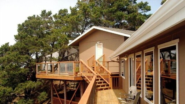 Une terrasse en bois avec un escalier menant à une zone abritée, le tout entouré d’arbres.