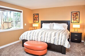 A bedroom with a large bed, two bedside tables with lamps, a window with a view of trees, and two wall-mounted artworks. - Ocean Grove Ocean View (Waldport)