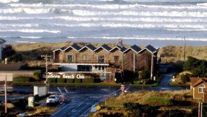 Une propriété située en bord de mer, appelée « Beachmore Beach Club », avec une rangée de cabanes, une route au premier plan et l’océan en arrière-plan.
