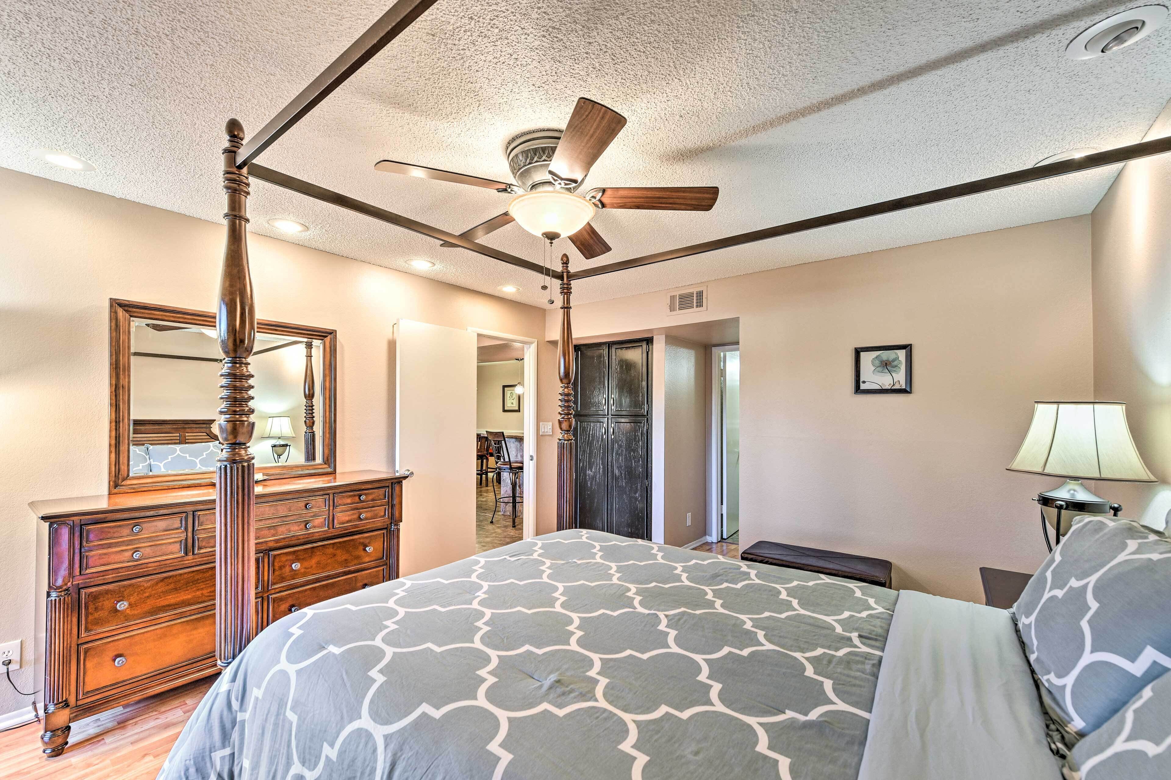 A bedroom with a four-poster bed, a ceiling fan, a dresser, and a mirror.