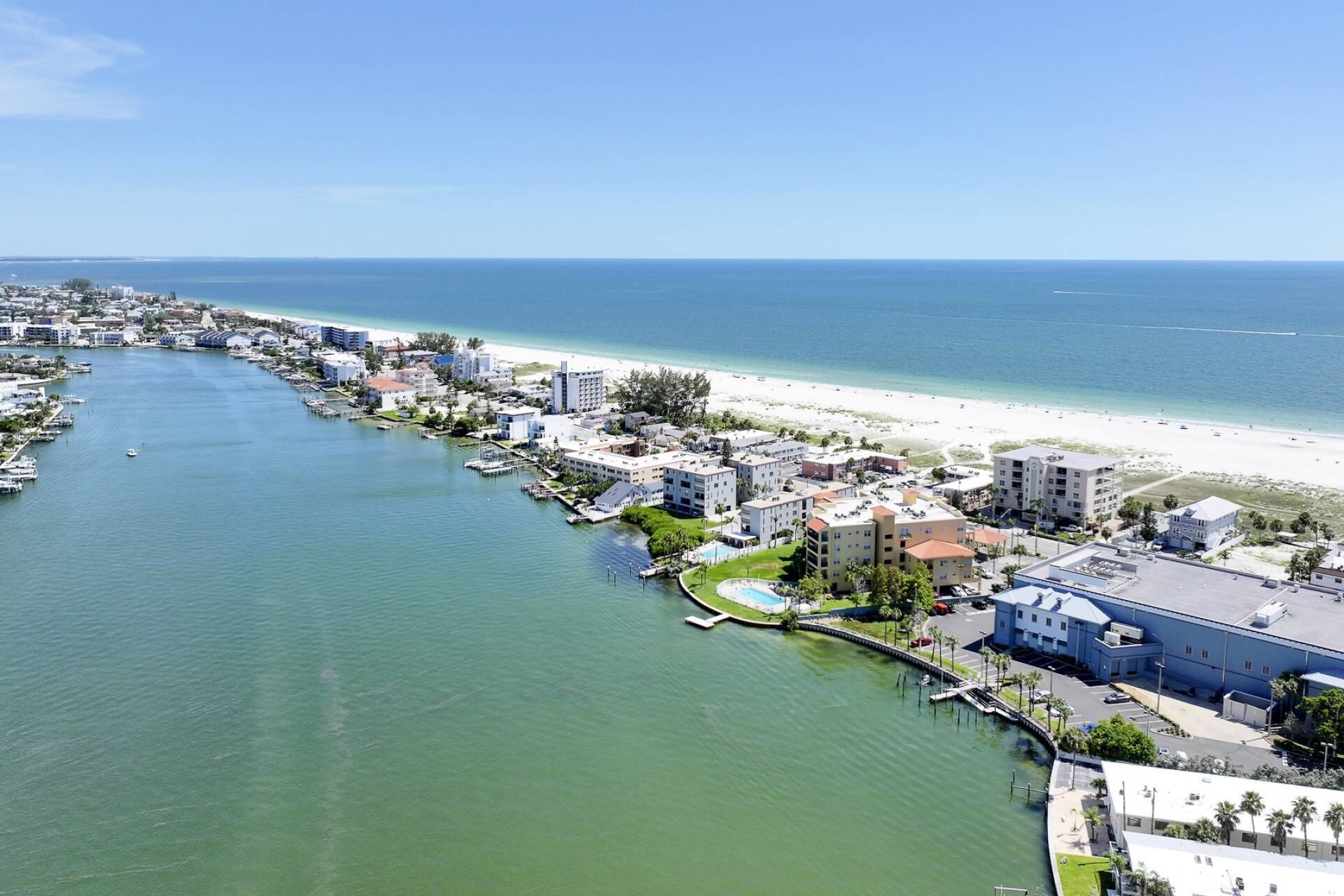 An aerial view of a coastal town with a marina, beachfront, and various buildings.