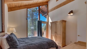 A bedroom with a bed, a wooden cabinet, a desk, and a window with a view of trees.