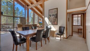 A spacious dining area with a wooden table and chairs, large windows offering a view of trees, and a framed poster on the wall.