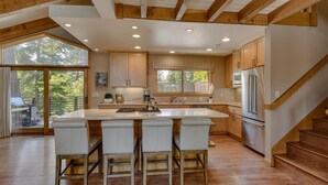 A spacious kitchen with a large island, wooden cabinets, and a view through the glass doors. - Forever Edgewood - Lakeview - TLUXP (Tahoe City)