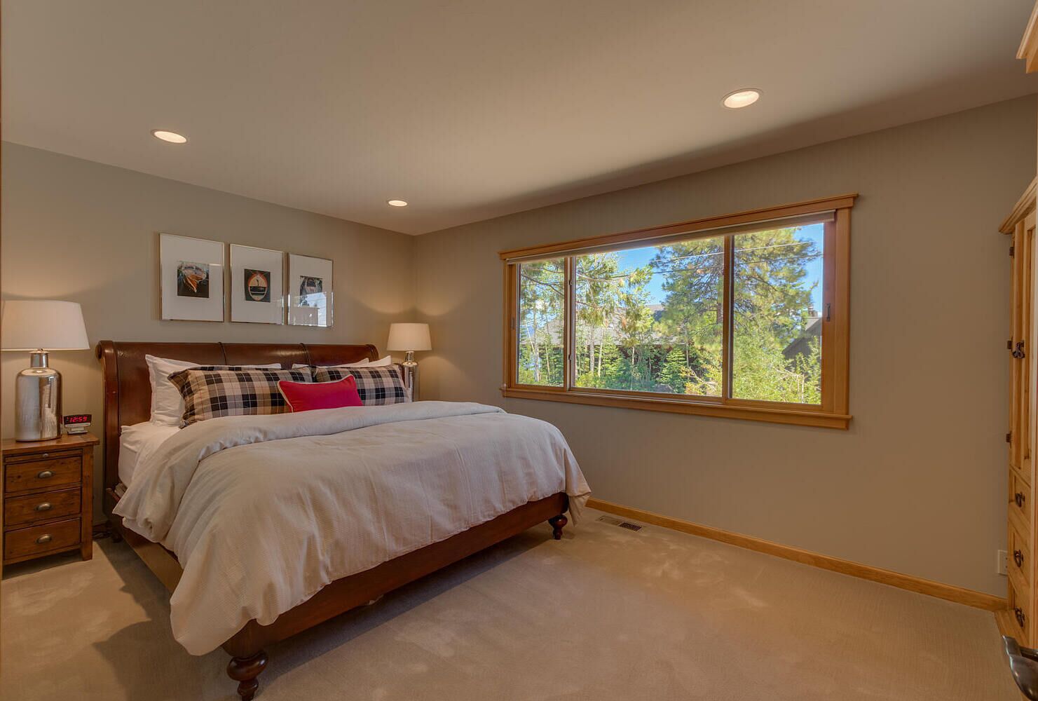 Une chambre à coucher avec un grand lit, deux tables de chevet, une commode et une fenêtre donnant sur des arbres.