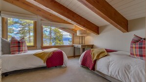 A bedroom with two beds, a desk, and a lamp. There are windows with a view of trees and mountains. - Forever Edgewood - Lakeview - TLUXP (Tahoe City)