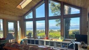 A room with large windows, a wooden ceiling, and a view of the ocean. - One Hundred Thousand Welcomes (Waldport)