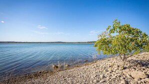 A clear view of a lake with a rocky shoreline and a single tree. - Playa del Sol: CL Lakefront + 3 Master Suites + Spacious Deck & Yard + Pool Table + Easy Lake Access (Canyon Lake)