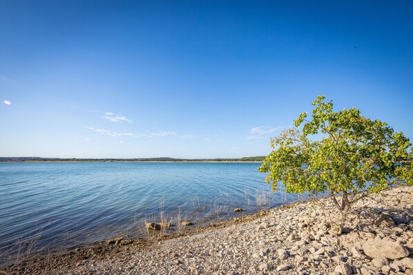 A clear view of a lake with a rocky shoreline and a single tree. - Playa del Sol: CL Lakefront + 3 Master Suites + Spacious Deck & Yard + Pool Table + Easy Lake Access (Canyon Lake)