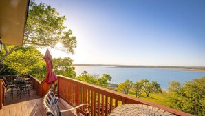 A wooden deck with outdoor furniture, a round table, and a view of a lake. - Playa del Sol: CL Lakefront + 3 Master Suites + Spacious Deck & Yard + Pool Table + Easy Lake Access (Canyon Lake)