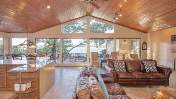 A spacious living area with a high ceiling, large windows, a ceiling fan, and a view of the outdoors. - Playa del Sol: CL Lakefront + 3 Master Suites + Spacious Deck & Yard + Pool Table + Easy Lake Access (Canyon Lake)