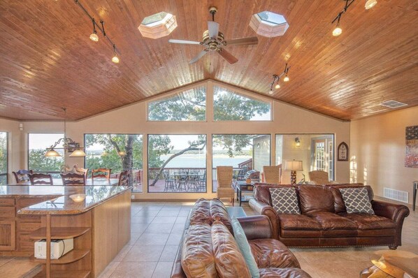 A spacious living area with a high ceiling, large windows, a ceiling fan, and a view of the outdoors. - Playa del Sol: CL Lakefront + 3 Master Suites + Spacious Deck & Yard + Pool Table + Easy Lake Access (Canyon Lake)