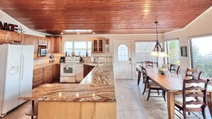 A kitchen with wooden cabinets, a granite countertop, and a dining area with a table and chairs. - Playa del Sol: CL Lakefront + 3 Master Suites + Spacious Deck & Yard + Pool Table + Easy Lake Access (Canyon Lake)