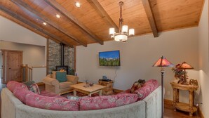 A cozy living room with a stone fireplace, wooden ceiling beams, and a large sofa.