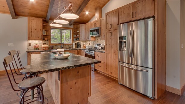 A modern kitchen with wooden cabinets, a large island with bar stools, stainless steel appliances, and pendant lighting.