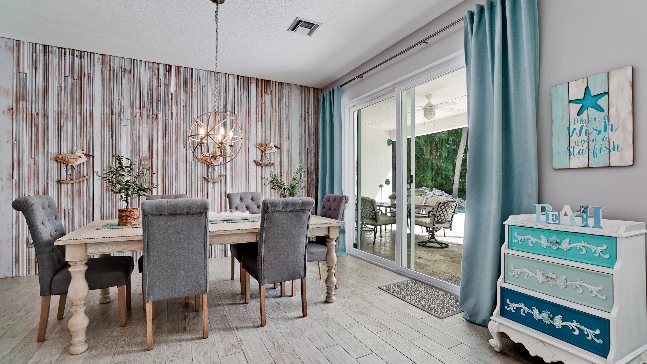 Un espace repas comprenant une table et des chaises en bois, un mur décoratif et une vue sur l’extérieur.