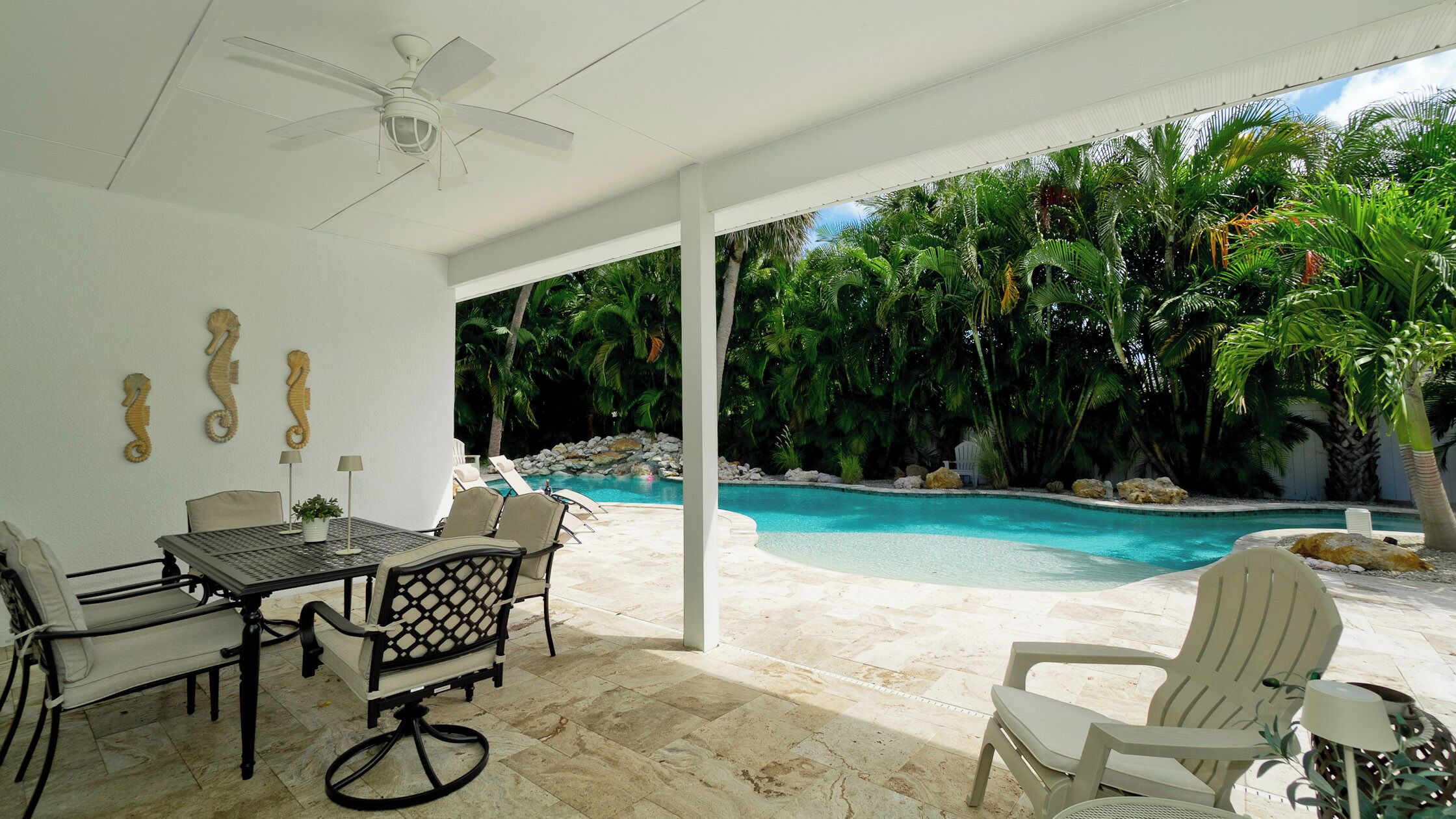 A covered outdoor area with a pool, lounge chairs, and a table with chairs.