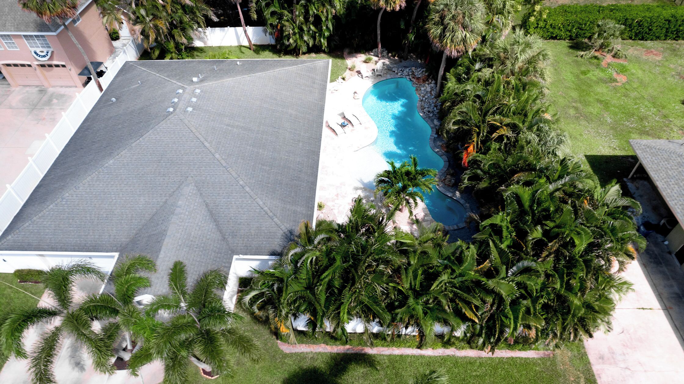 A residential property with a swimming pool, a covered patio, and lush tropical vegetation.