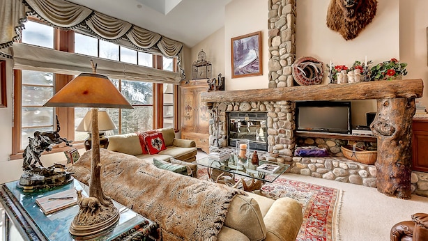 A cozy living room with a stone fireplace, a mounted bison head, and a large window with curtains.