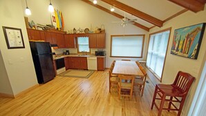 Una cocina con armarios de madera, un refrigerador, una mesa de comedor con sillas y un ventilador de techo.