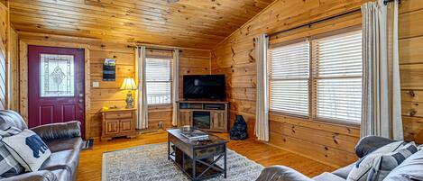 A cozy cabin interior with a wooden ceiling, a television, leather couches, and a red door.
