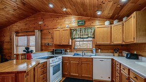 A wooden cabin-style kitchen with wooden cabinets, a microwave, stove, sink, and a dishwasher. - Bryson City Cabin w/ Hot Tub, Views & Pool Table! (Bryson City)