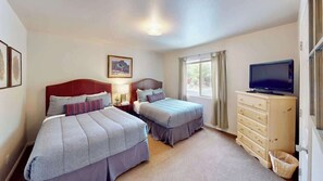 Une chambre d’hôtel avec deux lits, une télévision, une commode et une fenêtre avec des rideaux.
