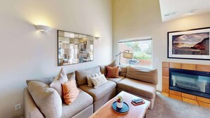 Una sala de estar con un sofá modular, una mesa de centro, una chimenea y un ventanal grande.