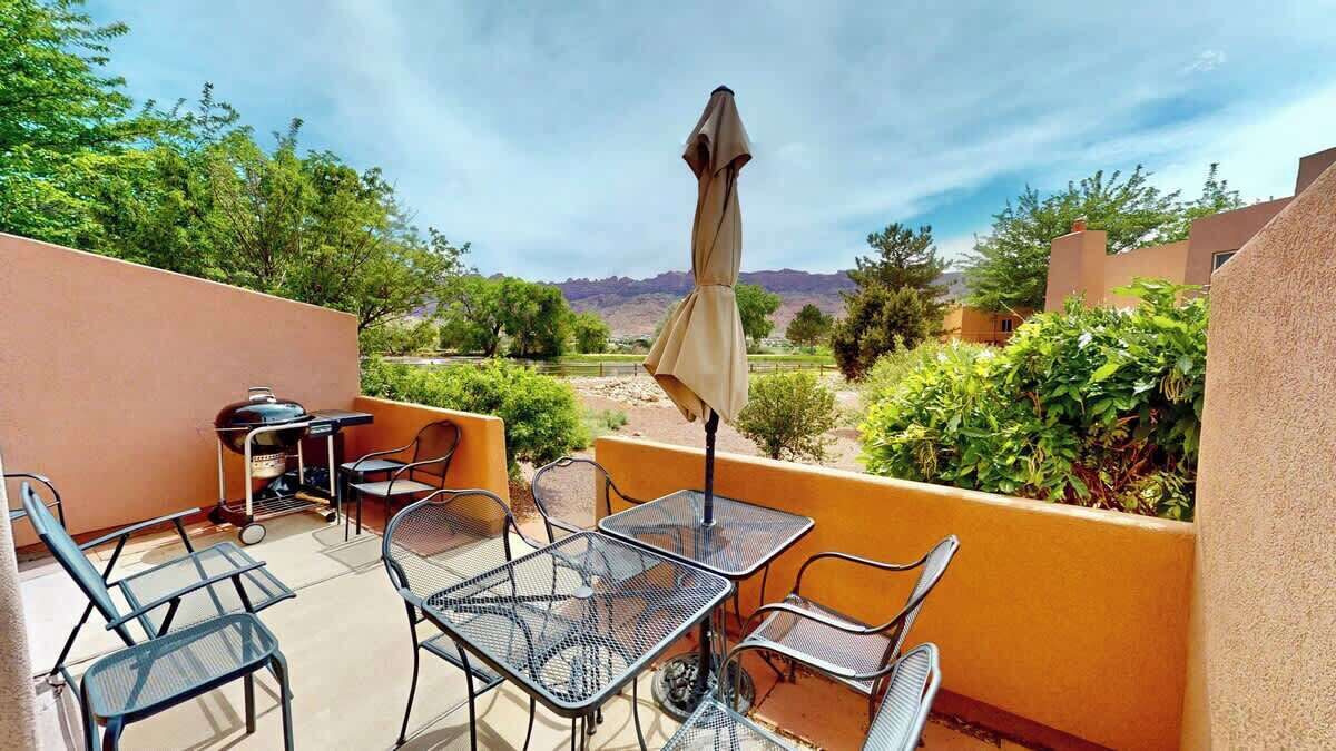 Une terrasse extérieure avec des tables et des chaises en métal, un barbecue et un parasol.