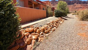 A building with a red exterior, a gravel pathway, and a rocky landscape in the background. - Saddle Creek - 3A1, 3 Bedroom 2 and a Half Bath Condo (Moab)