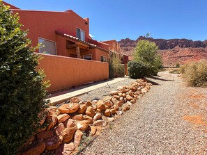 A building with a red exterior, a gravel pathway, and a rocky landscape in the background. - Saddle Creek - 3A1, 3 Bedroom 2 and a Half Bath Condo (Moab)