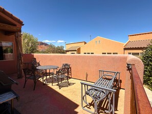 An outdoor patio with a round table and chairs, a barbecue grill, and a view of neighboring buildings.