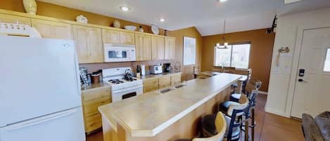 A kitchen with wooden cabinets, a white refrigerator, a stove, and a microwave. There is a bar area with stools.