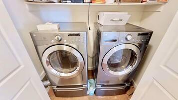 Dos lavadoras de carga frontal en un cuarto de lavado con un estante superior que contiene diversos objetos.