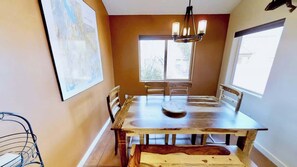 A dining area with a wooden table and chairs, a chandelier, and a window with a view.