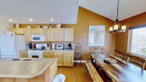A modern kitchen with wooden cabinets, a central island, and a dining area with a long table.