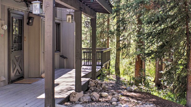 Una cabaña de madera con porche, escalones de piedra y un bosque de fondo.