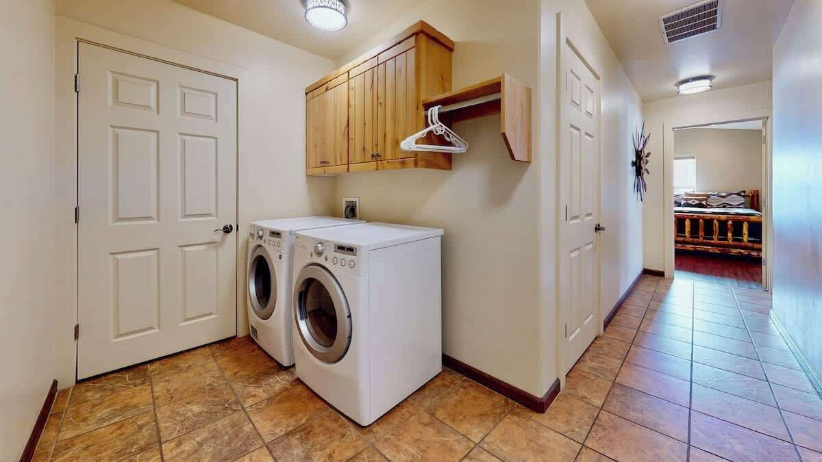 A laundry room with two front-loading washing machines, wooden cabinets, and a coat rack.