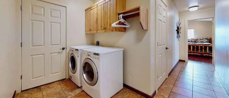 A laundry room with two front-loading washing machines, wooden cabinets, and a coat rack.