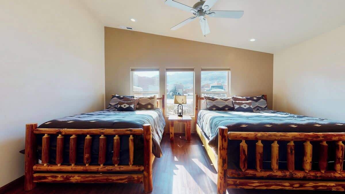 Une chambre avec deux lits en bois, un ventilateur de plafond et une fenêtre donnant sur un beau paysage.