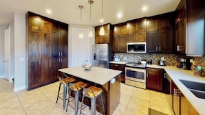A modern kitchen with dark wooden cabinets, stainless steel appliances, and a central island with bar stools. - Entrada at Moab - 668, Wolf Den (Moab)