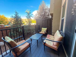 A balcony with outdoor furniture, a wooden fence, and a view of trees and a distant vehicle.