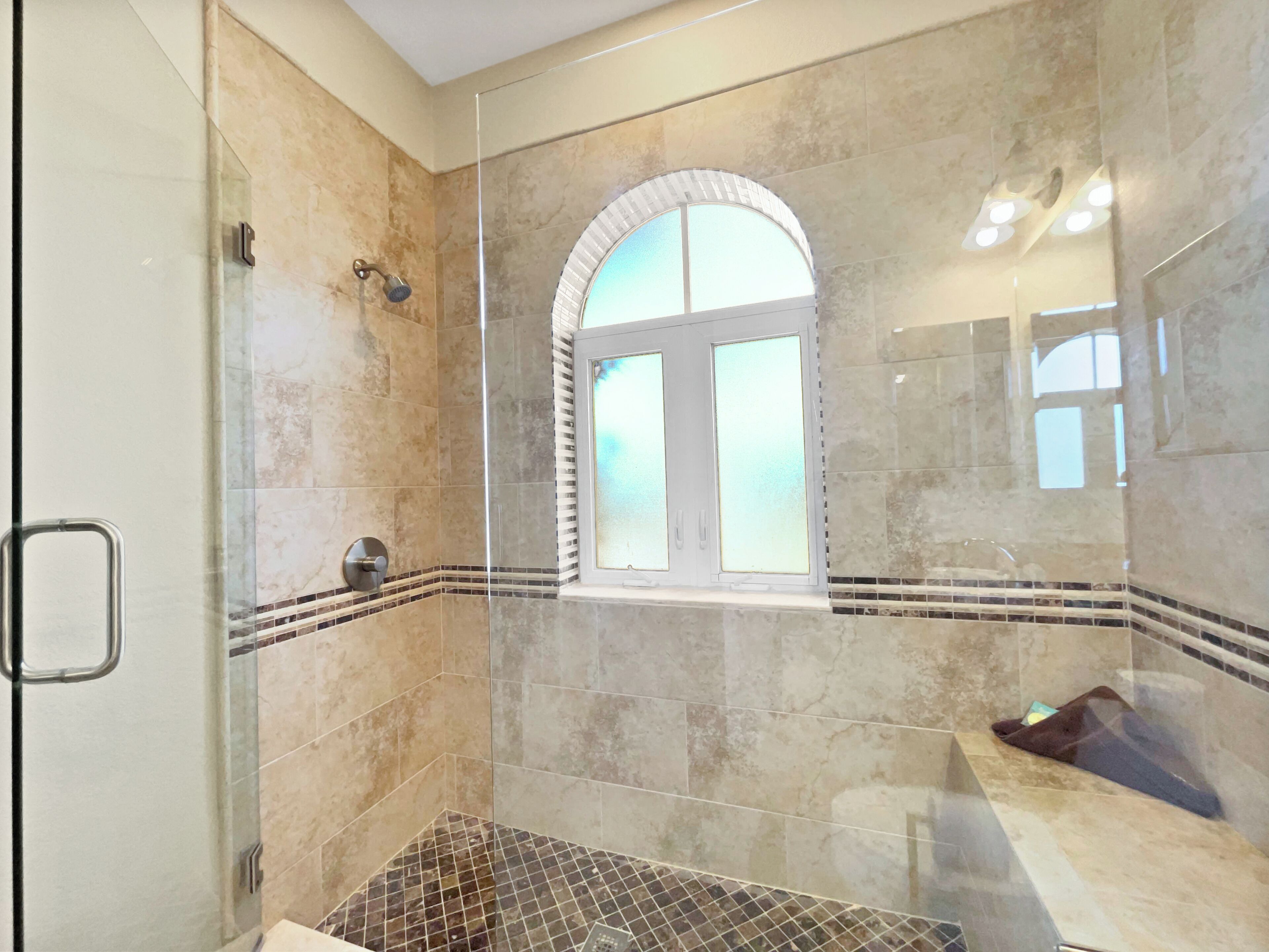 Un baño moderno con cabina de ducha de vidrio, suelo de baldosas y ventana con cristal satinado.