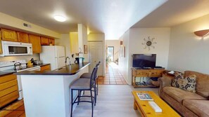 Un espace de vie compact comprenant un coin cuisine, un coin repas et un espace détente avec un canapé et une table basse.
