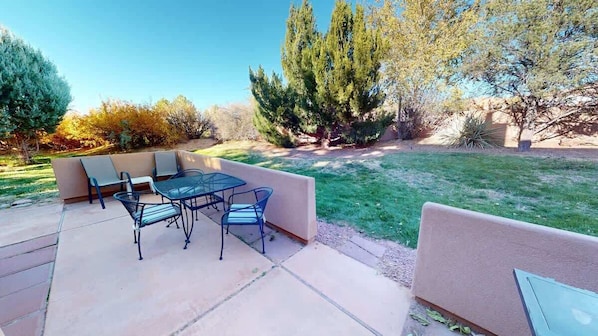 An outdoor patio with a table and chairs, surrounded by a grassy area and trees.