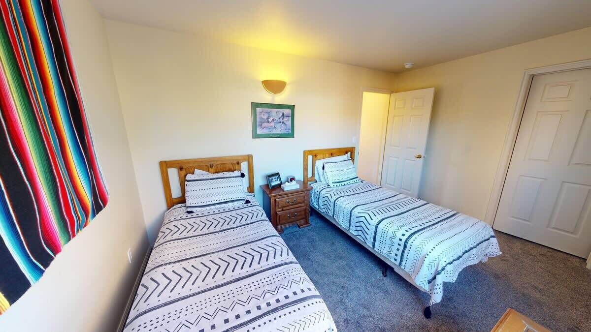Une chambre avec deux lits simples, une table de chevet avec une lampe et une porte.