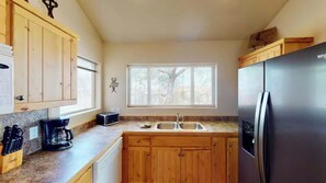 A kitchen with wooden cabinets, a stainless steel refrigerator, a coffee maker, and a window with blinds.