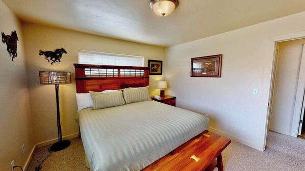 A bedroom with a bed, bedside lamp, wooden headboard, and a small table.